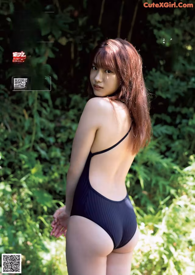 A woman in a black bathing suit standing in the woods.