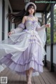 A woman in a purple and white dress is standing on a porch.