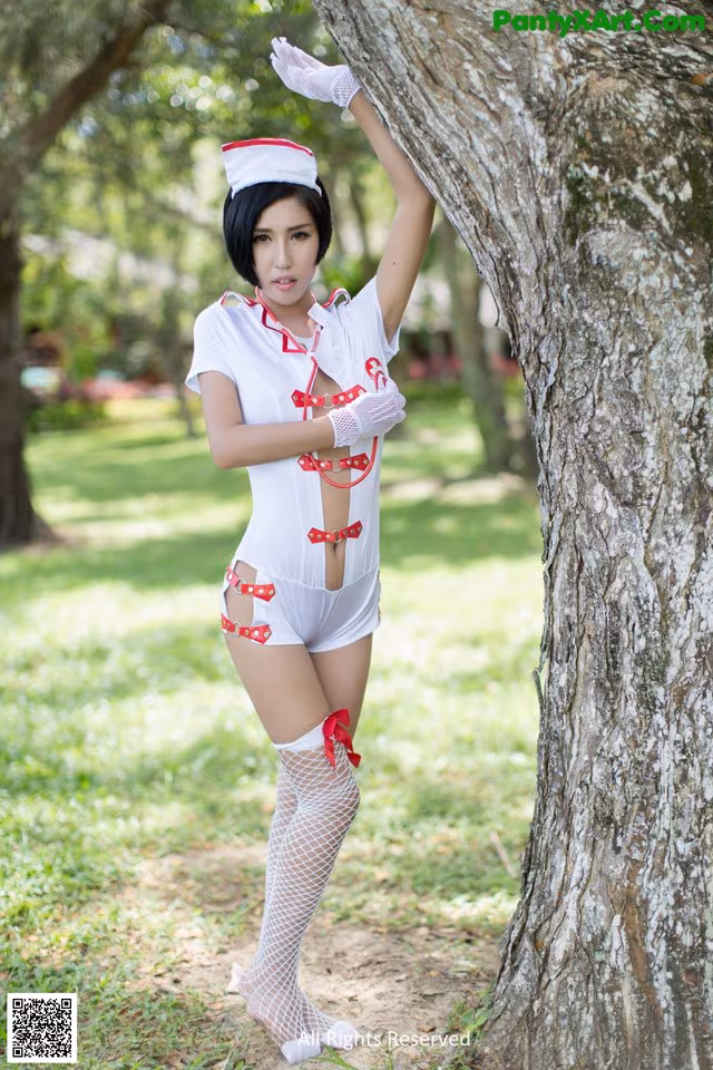 A woman dressed as a nurse leaning against a tree.