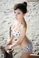 A woman in a bikini sitting on a log on the beach.