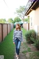 A woman walking down a sidewalk in a plaid shirt and jeans.