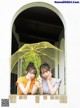 Two young women are looking out of a window with an umbrella.