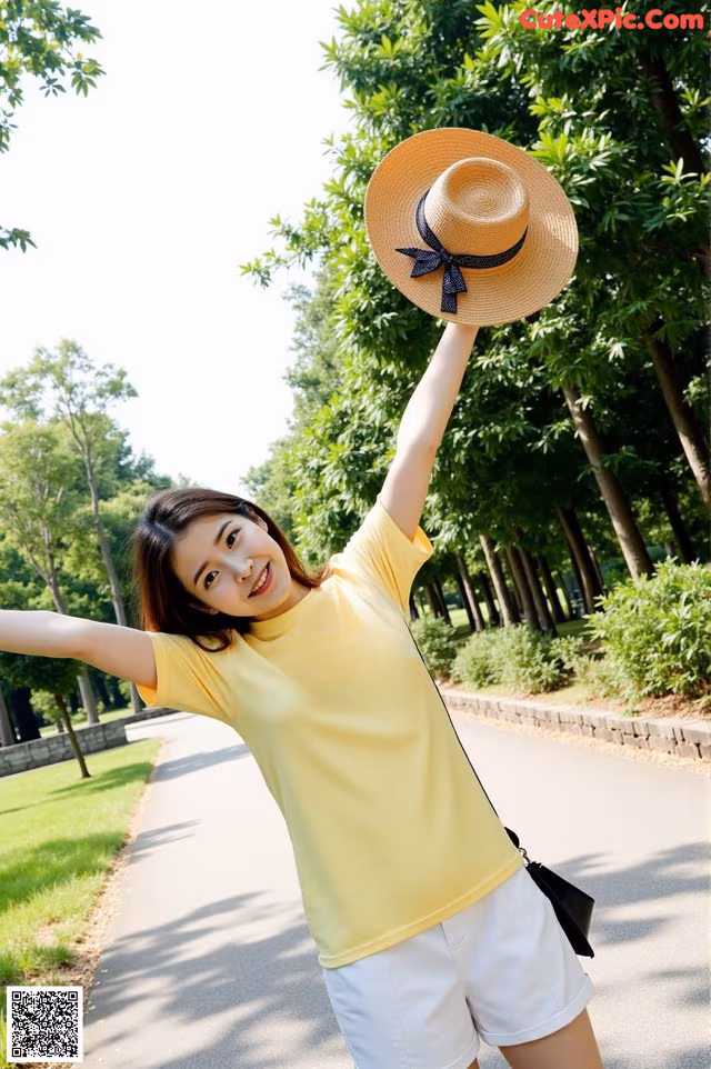 A woman in a yellow shirt and white shorts holding a straw hat.