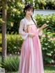 A woman in a pink and white hanbok standing in a garden.