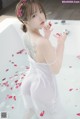 A woman in a white dress sitting in a bathtub with rose petals.