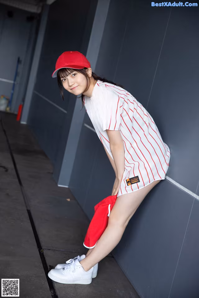 A woman leaning against a wall with a red hat on.