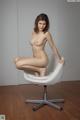 A nude woman sitting on a white chair.