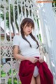 A woman in a white shirt and red skirt posing in front of a gate.