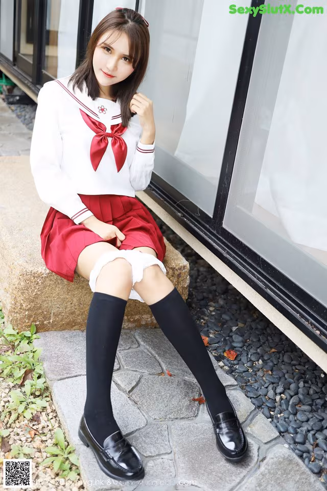 A woman in a school uniform sitting on a ledge.
