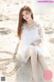 A woman in a white dress sitting on a sandy beach.