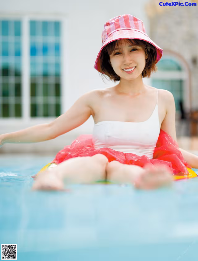 A woman in a pink hat sitting on an inflatable raft in a pool.