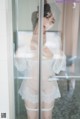 A woman in a white lingerie standing in front of a glass door.